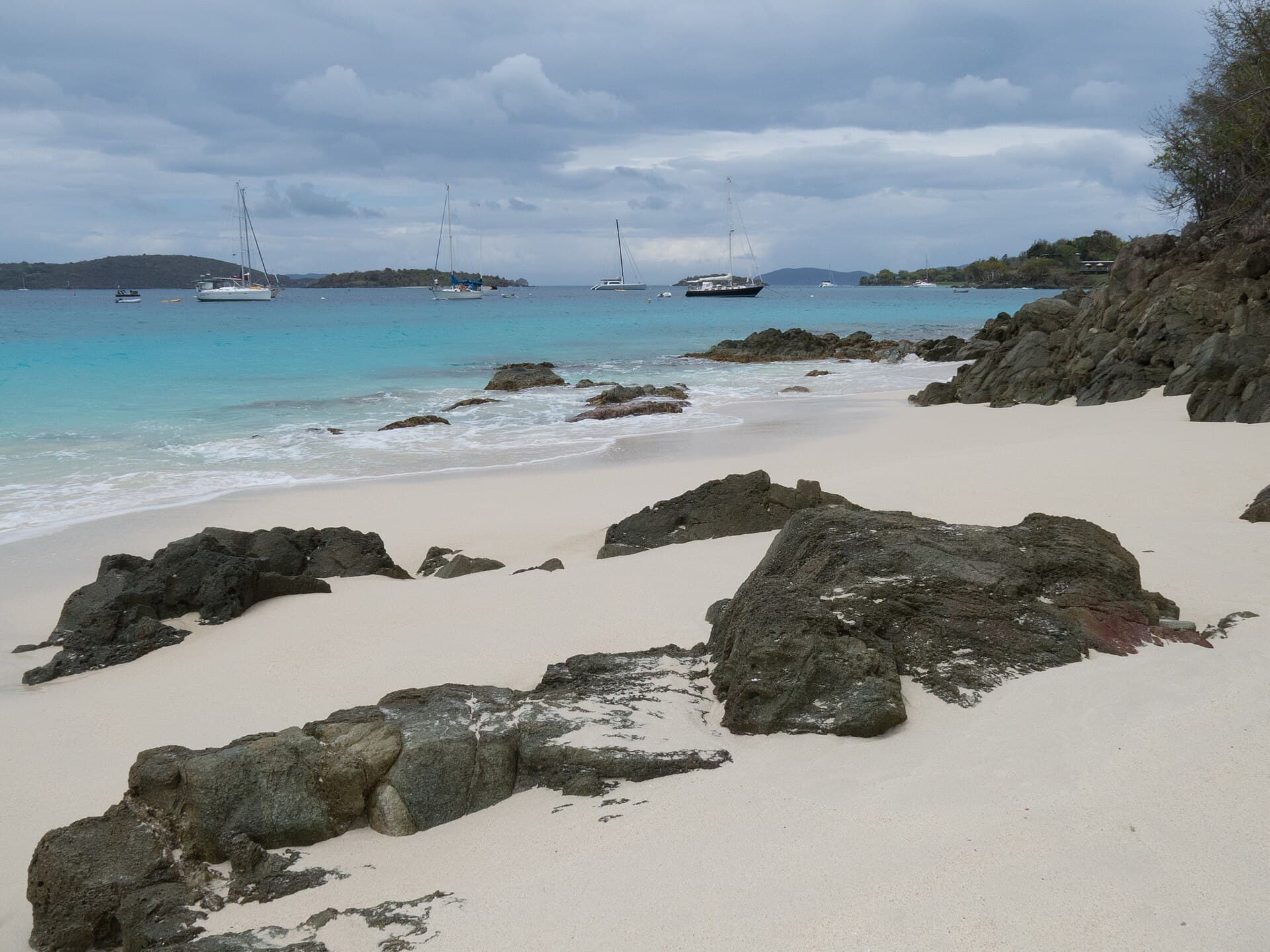 Sailboats moored off the white sand and dark rocks of Honeymoon Beach on St. John.