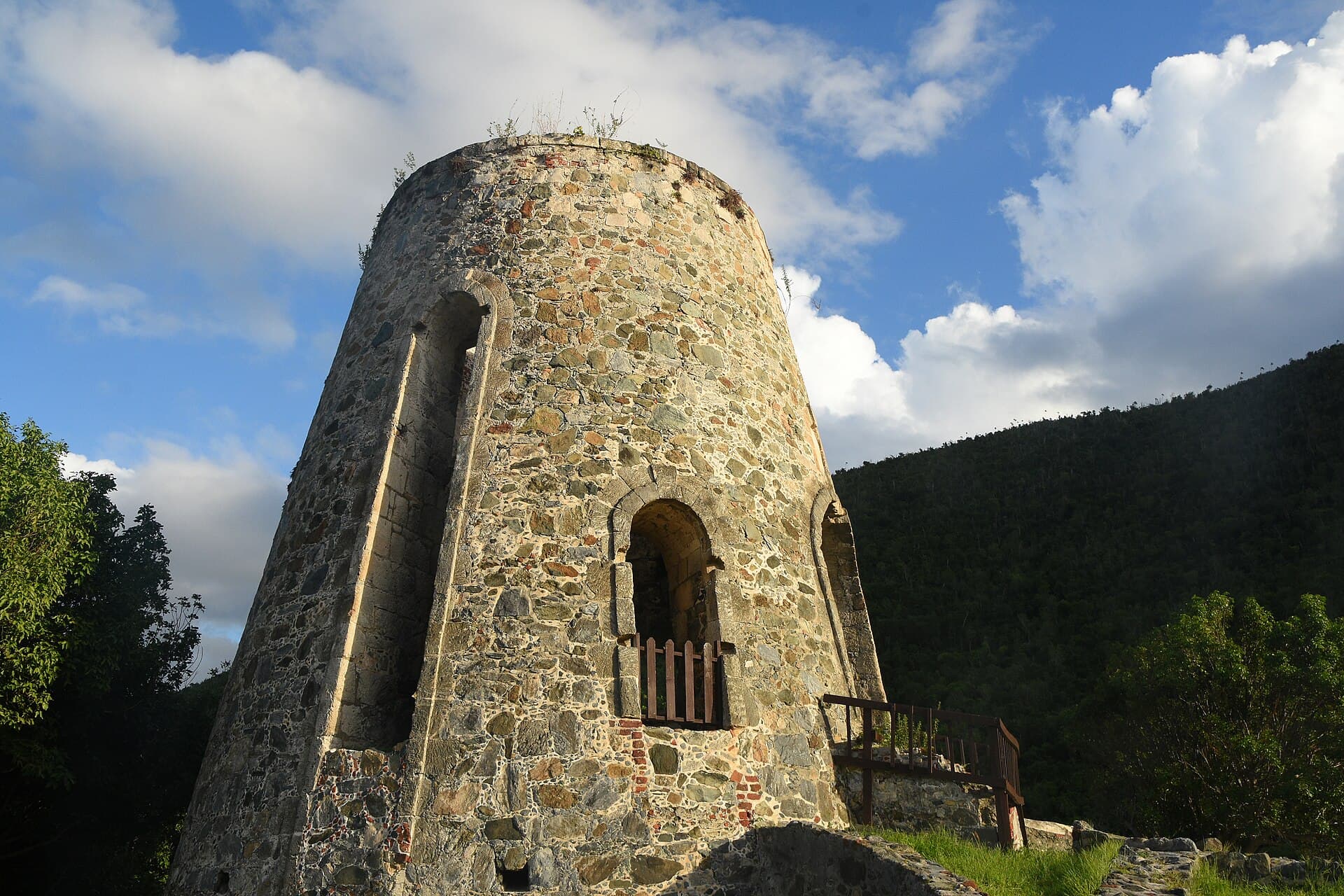 The stone windmill tower of the Annaberg Sugar Plantation ruins on St. John, against green hills.