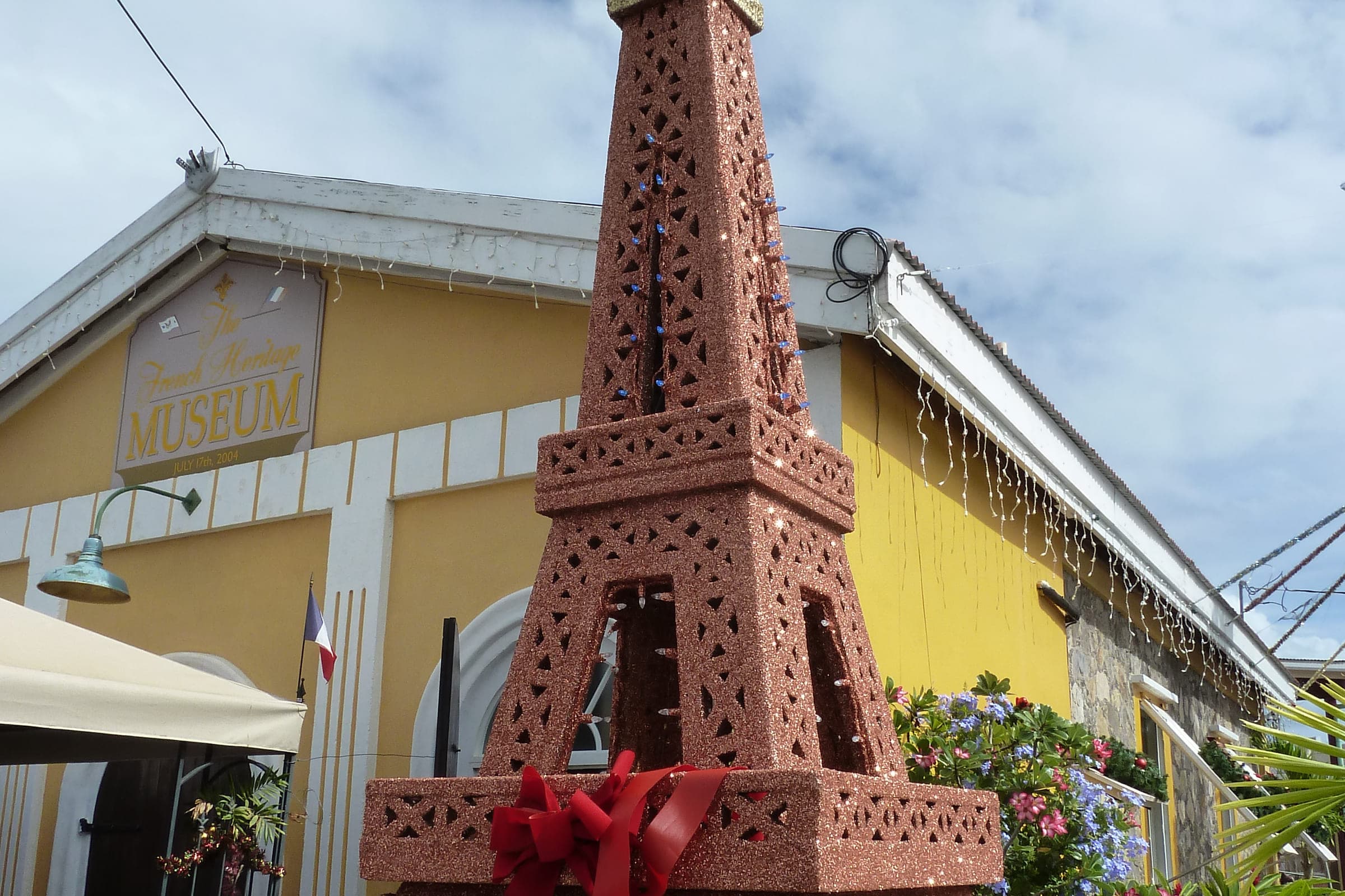 The yellow French Heritage Museum building in Frenchtown, St. Thomas, its painted museum sign and French flag beside the landmark decorative Eiffel Tower model, photographed in 2011.