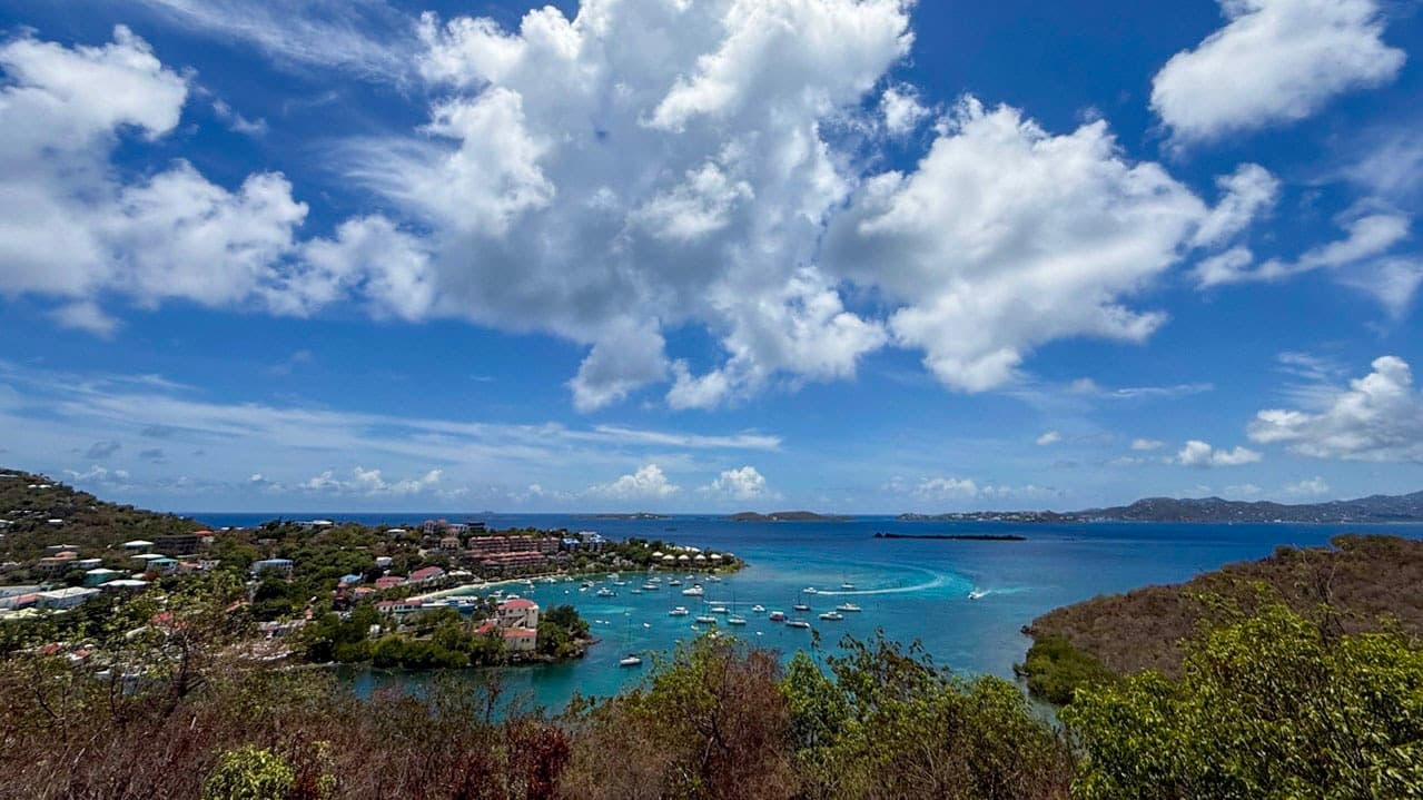 Wide overlook of Cruz Bay on St. John with boats, turquoise water, green hills, and towering clouds