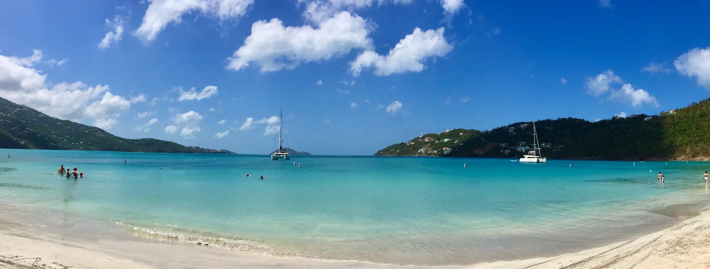 Beach-level panorama of Magens Bay on St. Thomas with calm turquoise water, white sand, and anchored catamarans