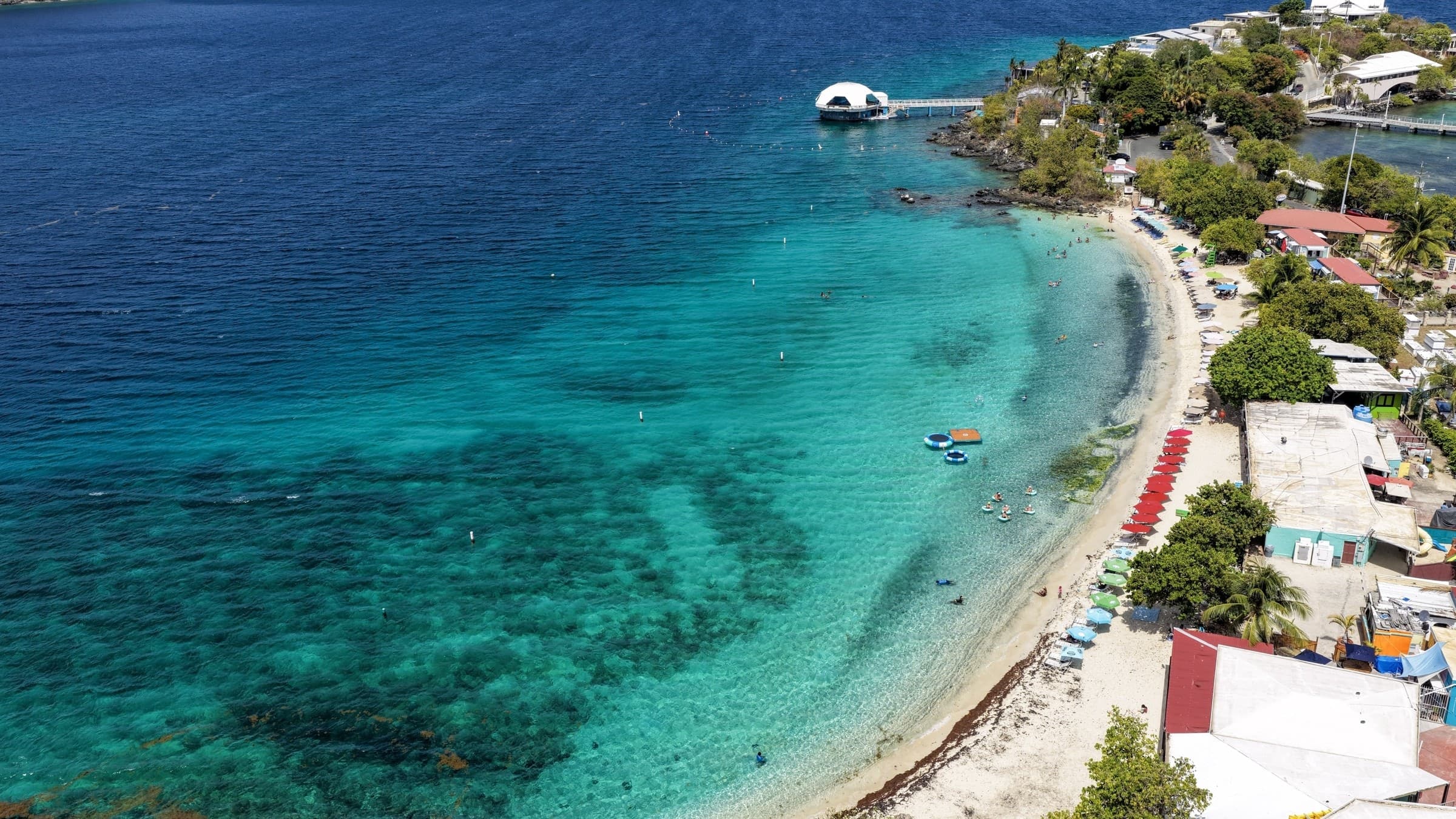 Aerial view along Coki Point Beach with clear turquoise water, swimmers, and the shoreline on St. Thomas.