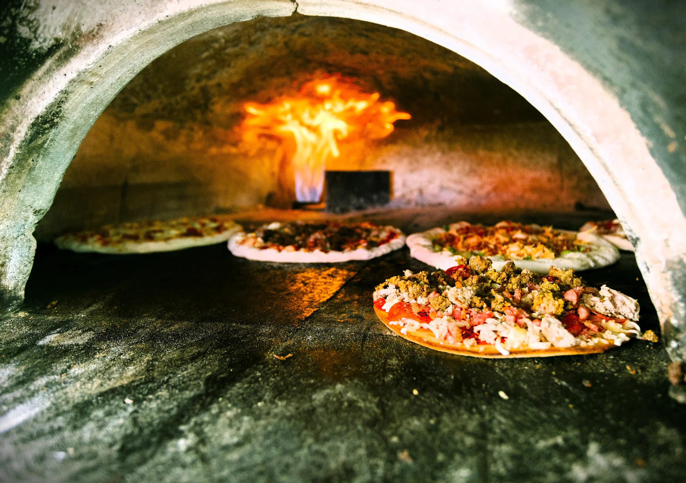 Pizzas cooking over flame inside The Mill's brick oven.