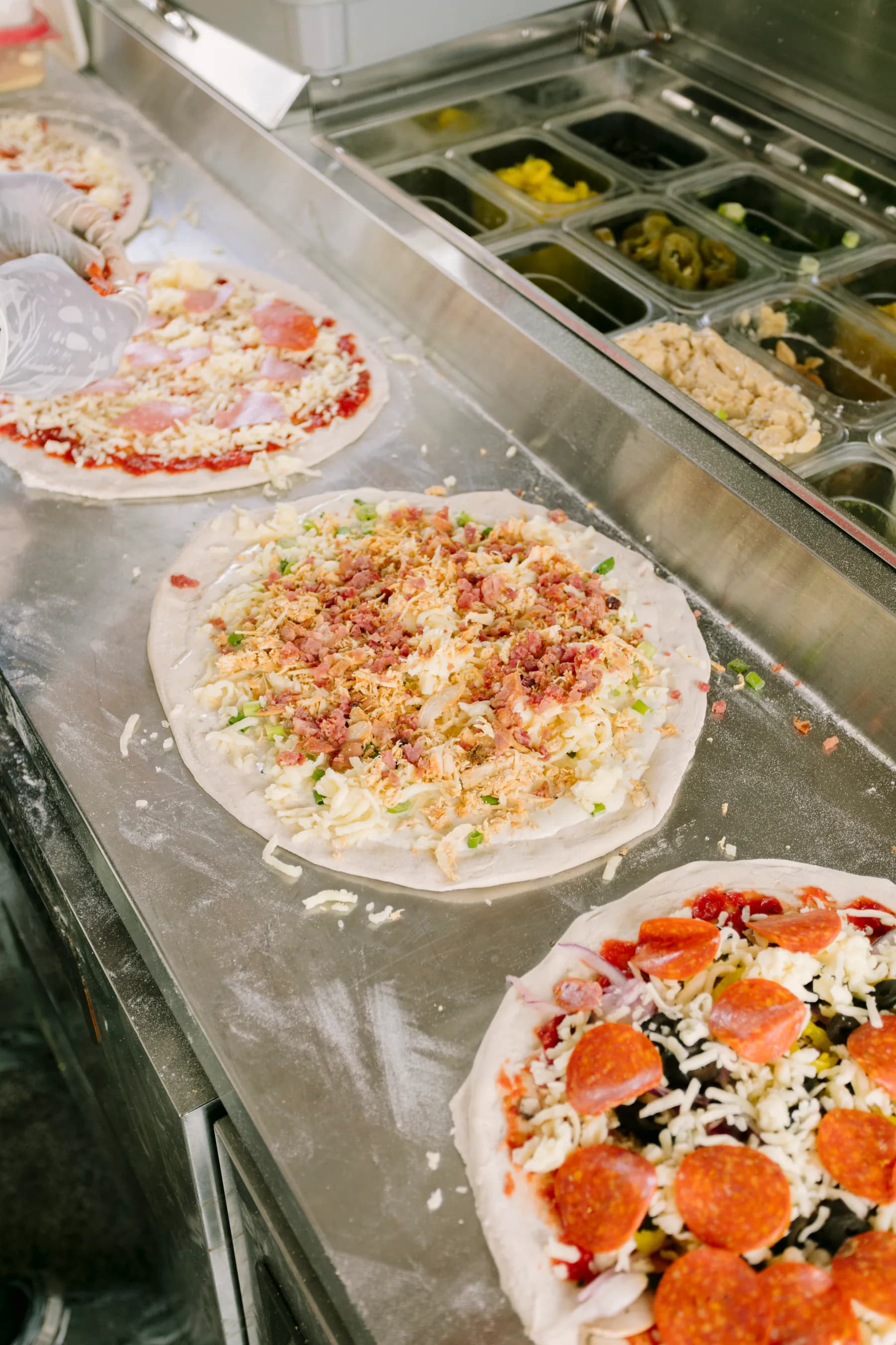 Several pizzas being topped at The Mill's preparation counter.